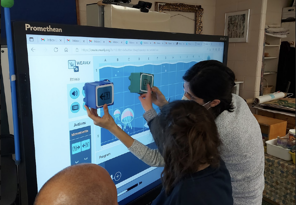 Two people planning a Weavly program using blocks and a Promethean board.