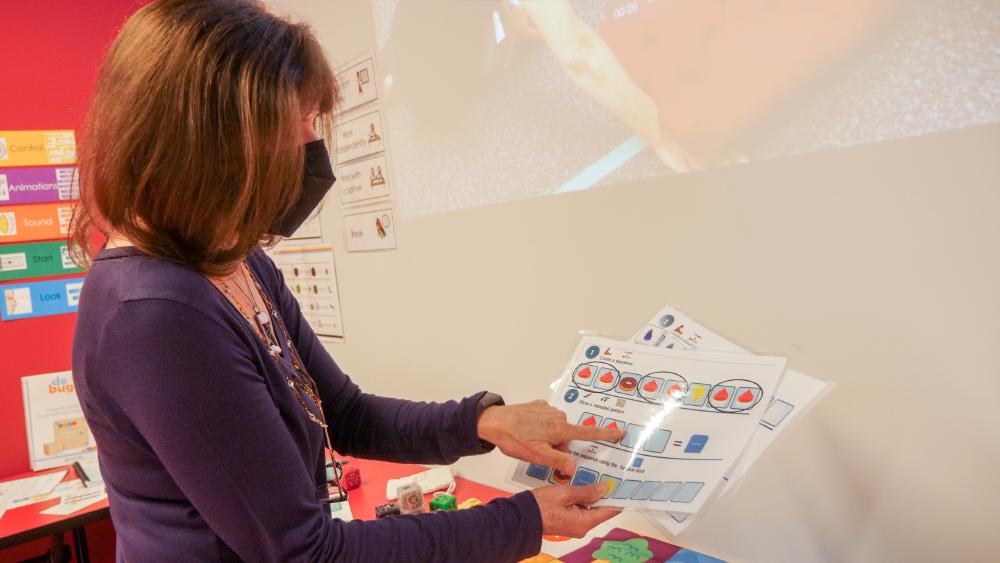 A woman is holding two brightly coloured coding curriculum sheets.